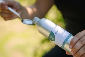 Georganics oil pulling mouthwash being poured into a spoon, ready for use in a natural outdoor setting.