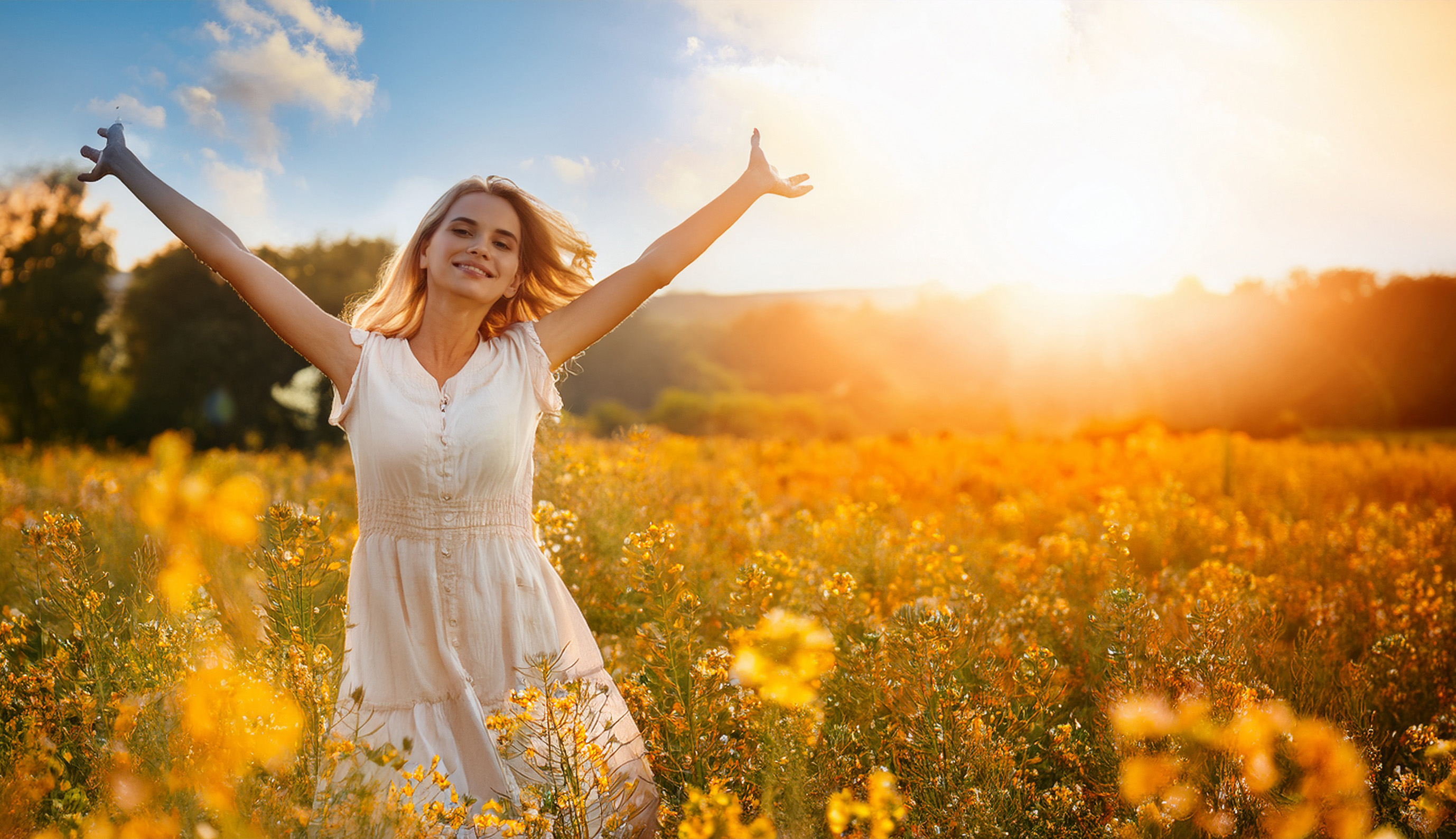 Woman standing in a sunlit field of flowers with open arms – representing vitality, heart energy, and summer strength in Traditional Chinese Medicine (TCM).
